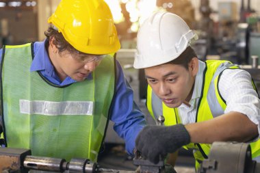 Üretim fabrikasında ekip olarak çalışan iki işçi, arka planda endüstri sahnesi, birlikte üretim faaliyetleri üzerinde çalışıyorlar.