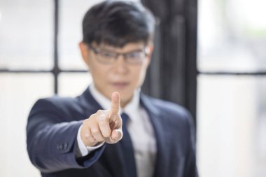 Takım elbiseli bir işadamı pencerenin önündeki kameraya işaret ediyor.