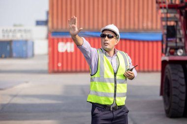 Konteyner Terminalinde telsiz kullanan sanayi işçisi konteynır yüklemesini kontrol ediyor.