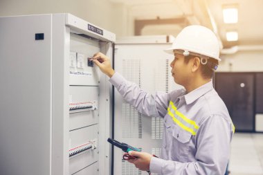 Elektrikçi bir erkek elektrik santrali bağlantı kutusunda çalışıyor. Çoklu ölçer ve devre kesicili kontrol paneli. Ana dağıtım panosundaki elektrik akımını çoklu klumetre ile ölçülüyor