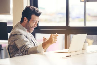 Meydan okumayı bitirdim! Çok mutlu bir iş adamı ofiste bir dizüstü bilgisayar kullanıyor. İş hayatında, işte ve okulda başarıya ulaşma fikri. İnsan muzaffer bir bireydir. Online bahis konsepti.