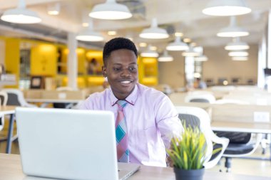 Çalışan bir ortamda dizüstü bilgisayar kullanan siyahi bir adamın portresi. Ya Afrikalı bir işadamı ya da öğrenci..