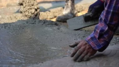 İnşaat işçisinin eldivenli ellerini yakın mesafeden kazımak için mala kullanarak yeni dökülmüş beton bloknotlarla karıştırın.