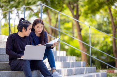 Kampüste, sıradan giyinmiş muhteşem bir çift dışarıda merdiven boşluğunda otururken dizüstü bilgisayar kullanıyor..