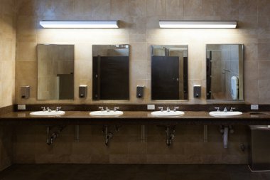 Çoklu lavaboları, muslukları, sabunlukları ve aynaları olan temiz kaplamalı modern umumi tuvaletin verimliliği.