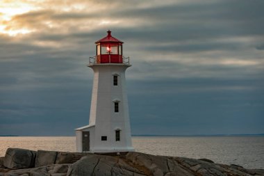 Famous tourist attraction Peggy's Cove Lighthouse on granite rock cliffs overlooking calm Atlantic Ocean, Nova Scotia, NS, Canada clipart