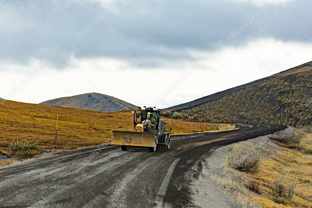 Grader road maintenance heavy equipment on gravel dirt road of remote Dempster Highway in arctic tundra landscape of northern Yukon Territory, YT, Canada