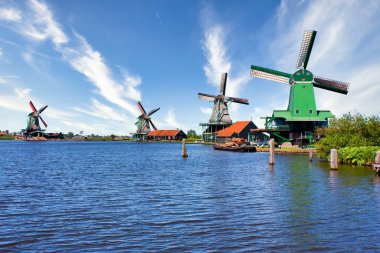ZAANSE SCHANS, NETHERLANDS - CRCA AĞUSTOS 2020: Hollanda yel değirmeni Amsterdam yakınlarında, mavi gökyüzü ve nehir suyuyla.