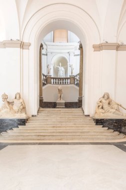 Napoli Arkeoloji Müzesi 'nin içindeki merdiven manzarasında klasik mimari, mermer heykeller ve zarif eğimli tasarım yer alıyor..