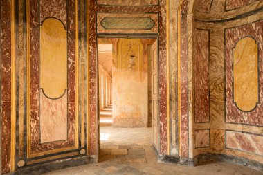 Agli Kalesi 'nin iç manzarasında boyalı duvarlar, eski mermer dokular ve güneşli bir koridora açılan kapılar, İtalyan kraliyet mirası ve mimarisini sembolize ediyor..