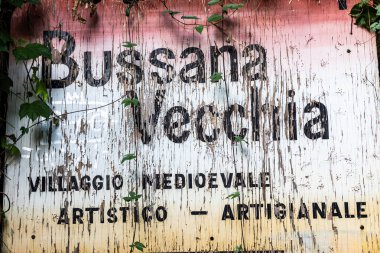 BUSSANA VECCHIA, ITALY AUGust 2025 Liguria 'nın ortaçağ sanatsal ve sanatsal köyü Bussana Vecchia' nın girişindeki ahşap tabela, dağcılık bitkileri ve kırsal cazibeyle çevrili..
