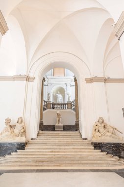 Napoli Arkeoloji Müzesi 'nin içindeki merdiven manzarasında klasik mimari, mermer heykeller ve zarif eğimli tasarım yer alıyor..