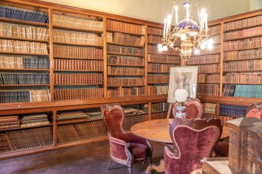 AGLI, ITALY NOVEMBER 2025 Castello di Agli 'deki eski kütüphanenin içi 18. yüzyıl atmosferini ve zarafetini koruyan antika ahşap kitaplıklar, kırmızı kadife sandalyeler ve bir avize gösteriyor..