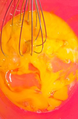 Yemek pişirme süreci. Kırmızı bir kasede, çırpıcıyla yumurtaları çırp.