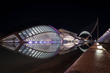 VALENCIA, İspanya - 6 Şubat 2025: L 'Hemisferic, Valencias Sanat ve Bilim Şehri' nin en ikonik yapılarından biri, geceleyin aydınlatıldı ve etrafındaki durgun suya mükemmel bir şekilde yansıdı..
