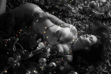 Beyaz iç çamaşırlı güzel, seksi esmer kız Noel ağacında yatıyor.