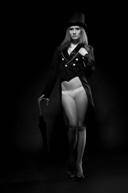 Siyah ceketli, güzel, seksi esmer kız. Siyah bir arka planda çıplak ve silindir gibi duruyor.