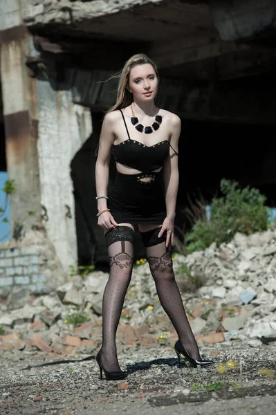 穿着黑色连衣裙和长袜的漂亮性感金发姑娘在废墟的背景下摆姿势 — 图库照片