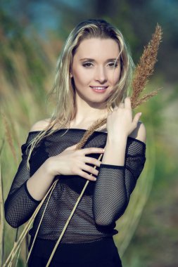 Siyah bluzlu güzel sarışın kız sazlıklar içinde poz veriyor.