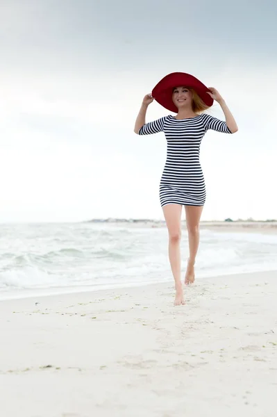 Güzel Sarışın Çizgili Elbiseli Kırmızı Şapkalı Güzel Kız Plaj Boyunca — Stok fotoğraf