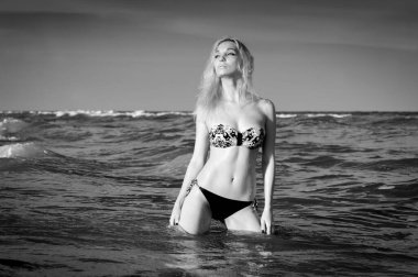 Suyun yakınındaki kumlu bir sahilde mayo giymiş güzel sarışın kız.