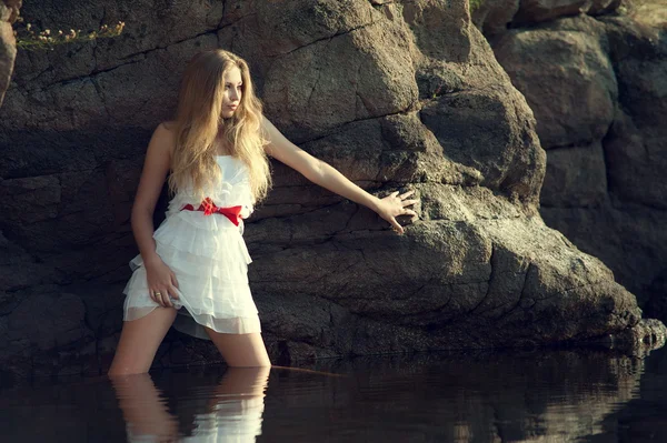 Menina loira na água encostada na rocha — Fotografia de Stock