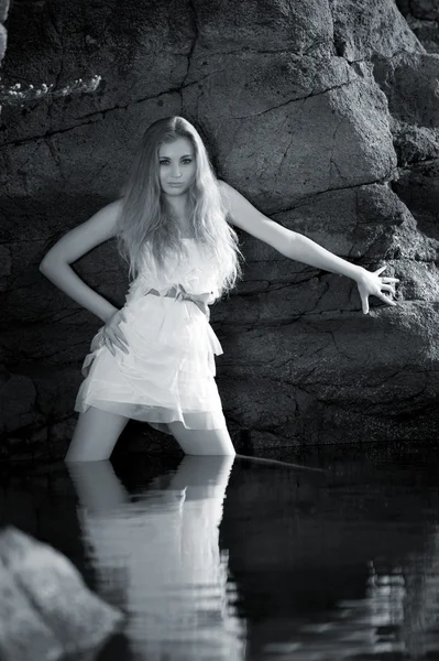 Blond tjej i vattnet lutande på rock — Stockfoto