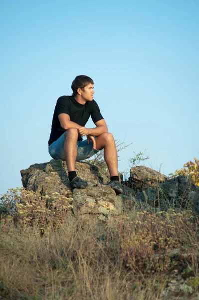 Junger Mann sitzt auf Felsen — Stockfoto