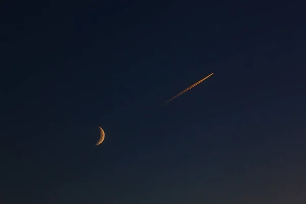 The flight of a passenger plane near the moon in the evening sky after sunset.