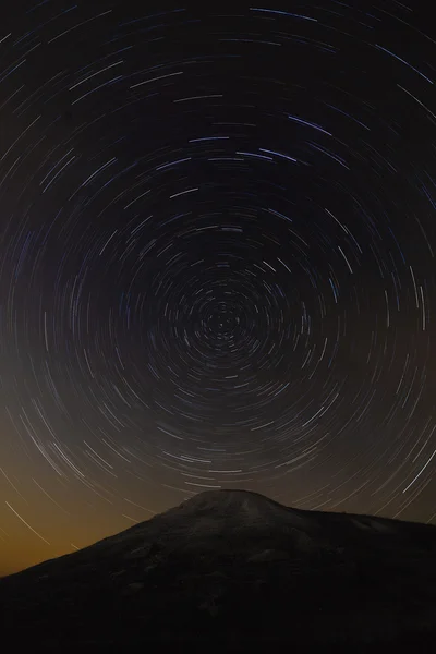 Trail of stars around the pole star on top of the mountain backg