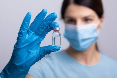 Koruyucu eldivenleri ve maskesiyle doktor bilim adamı elinde aşı ilacı dozajı fotoğrafı tutuyor.