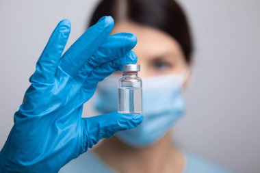 Koruyucu eldivenleri ve maskesiyle doktor bilim adamı elinde aşı ilacı dozajı fotoğrafı tutuyor.
