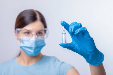 Koruyucu eldivenli ve maskeli bir doktor cam şişeyi enjeksiyon sıvısıyla tutuyor. Grip ve koronavirüse karşı aşı. Stok fotoğrafı