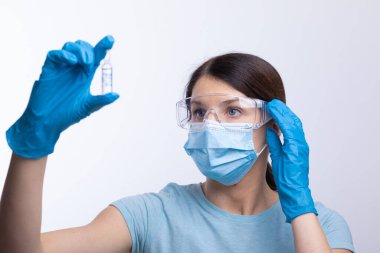 Koruyucu eldivenli ve maskeli bir doktor cam şişeyi enjeksiyon sıvısıyla tutuyor. Grip ve koronavirüse karşı aşı. Stok fotoğrafı