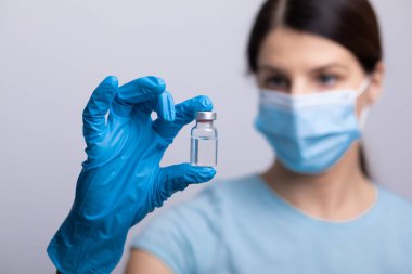 Koruyucu eldivenleri ve maskesiyle doktor bilim adamı elinde aşı ilacı dozajı fotoğrafı tutuyor.