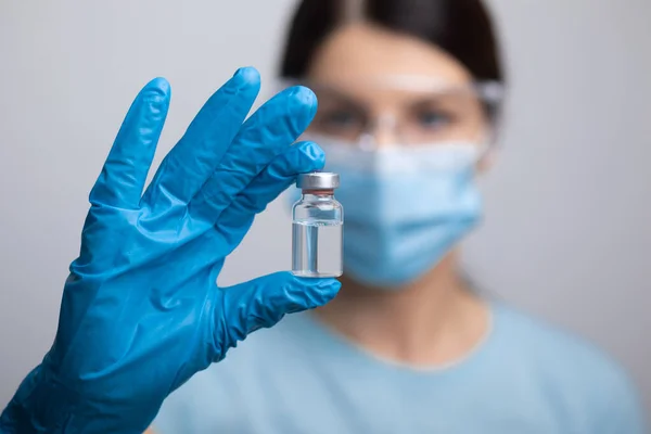 Doctor Scientist in protective gloves and mask holding glass vial with injection liquid. Vaccination against influenza and coronavirus. Stock photo