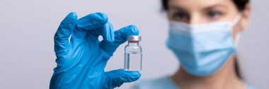 Koruyucu eldivenleri ve maskesiyle doktor bilim adamı elinde aşı ilacı dozajı fotoğrafı tutuyor.