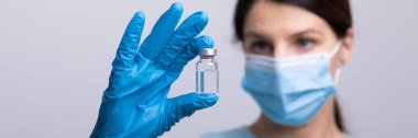 Koruyucu eldivenleri ve maskesiyle doktor bilim adamı elinde aşı ilacı dozajı fotoğrafı tutuyor.