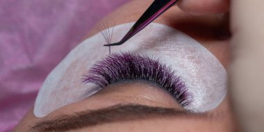 Cımbızla uzatılmış mor kirpiklerle iyileştirme güzellik prosedürü. Uzun renkli kirpikli kadın gözleri.