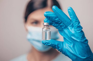 Koruyucu eldivenleri ve maskesiyle tıbbi bilimadamı elinde aşı ilacı dozajı fotoğrafı tutuyor.