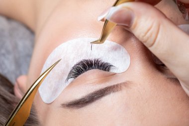 Kirpiklerin yakın plan güzellik prosedürü. Cımbızla uzatılmış uzun kirpikli kadın gözleri.