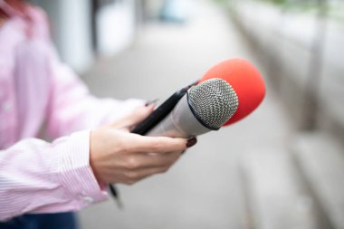 Etkinlikte çalışan profesyonel kadın gazeteci, elinde mikrofon tutuyor ve akıllı telefon diktafonuna notlar kaydediyor.