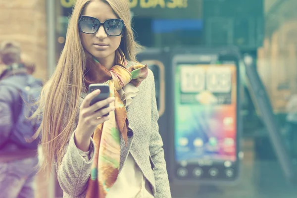 Jovem mulher elegante com smartphone andando na rua — Fotografia de Stock