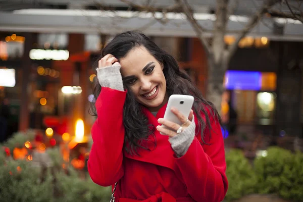 Vrouw in rode jas met mobiele telefoon in handen, smartphone, stedelijke — Stockfoto