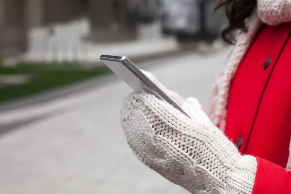 Frau in rotem Mantel mit Smartphone in der Hand geht durch die Stadt — Stockfoto