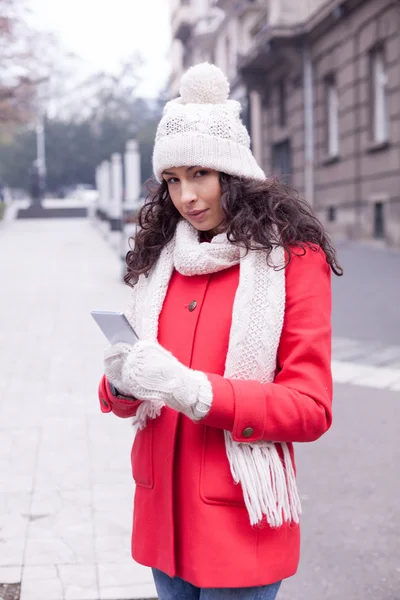 Beautiful woman in red coat and wool cap and gloves with smartph — Stock Photo, Image