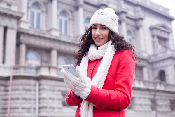 Beautiful woman in red coat and wool cap and gloves with smartph — Stock Photo, Image