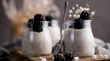 Böğürtlenli Chia pudingi, karanlık bir masada cam kavanozlarda üç porsiyon..