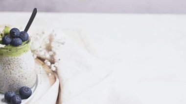 Kivili Chia pudingi, yabanmersini ve hindistan cevizi dilimleri, beyaz bir masada cam kavanozlarda üç porsiyon..