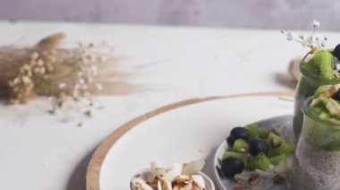 Kivili Chia pudingi, yabanmersini ve hindistan cevizi dilimleri, beyaz bir masada cam kavanozlarda üç porsiyon..